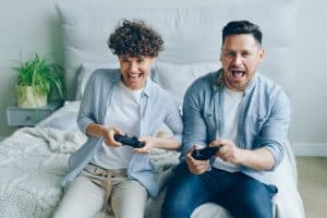 free photo of a couple sitting on a bed and playing a video game