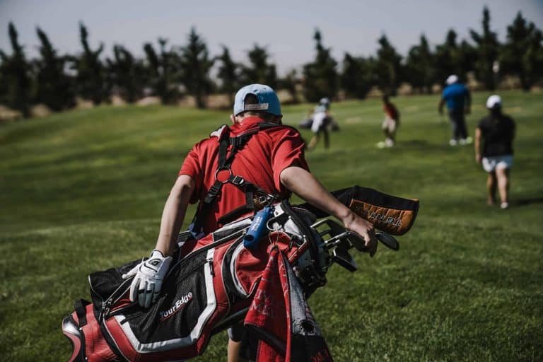 A golfer in red carrying a bag on a lush green golf course during a sunny day./VR headsets