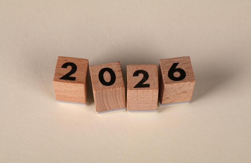 Wooden blocks display the number 2026, arranged unevenly against a neutral background. The image conveys a sense of anticipation for the future.