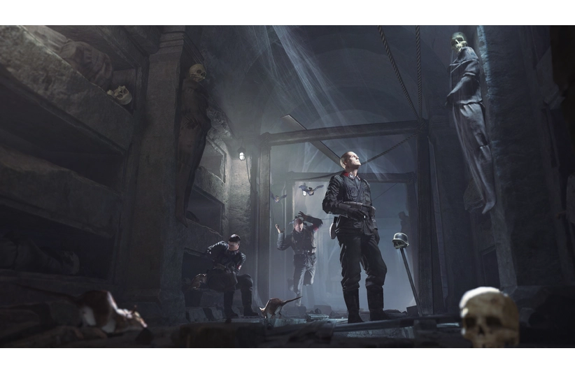 A dimly lit crypt with three soldiers in tactical gear, cautiously exploring. The atmosphere is eerie, with skeletons in alcoves and skulls on the floor. Wolfenstein: The Old Blood, Courtesy of MachineGames and Bethesda Softworks. This is not footage of Wolfenstein 3.