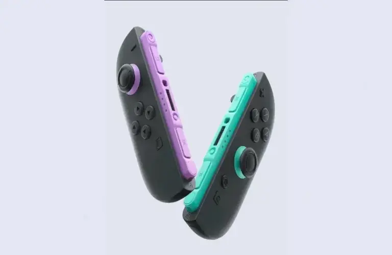 Two new Nintendo Switch 2 Joy Con controllers, one with a purple grip and the other with a teal grip, face each other against a light background, creating a playful tone.